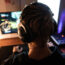 Rear View of Gamer with Headset on Playing Online Video Games in Dark Room